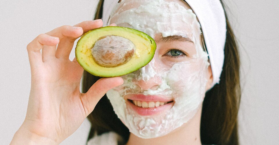 woman wearing a diy beauty mask and holding an avocado