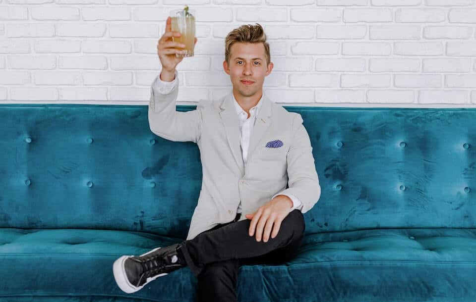 man on blue couch holding up a glass to celebrate his affiliate marketing revenue