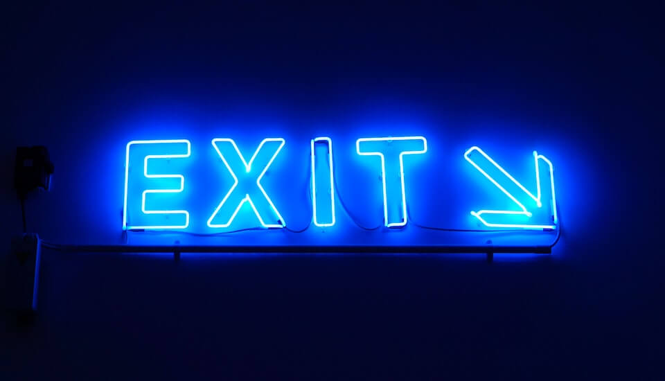 blue glowing exit sign and arrow against black background