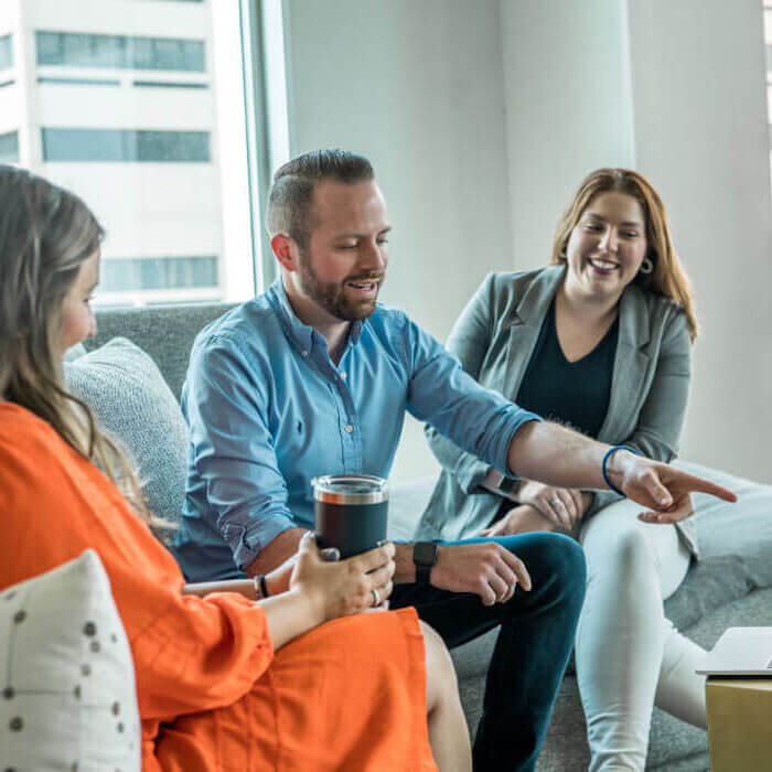 man sitting on couch pointing with two women watching