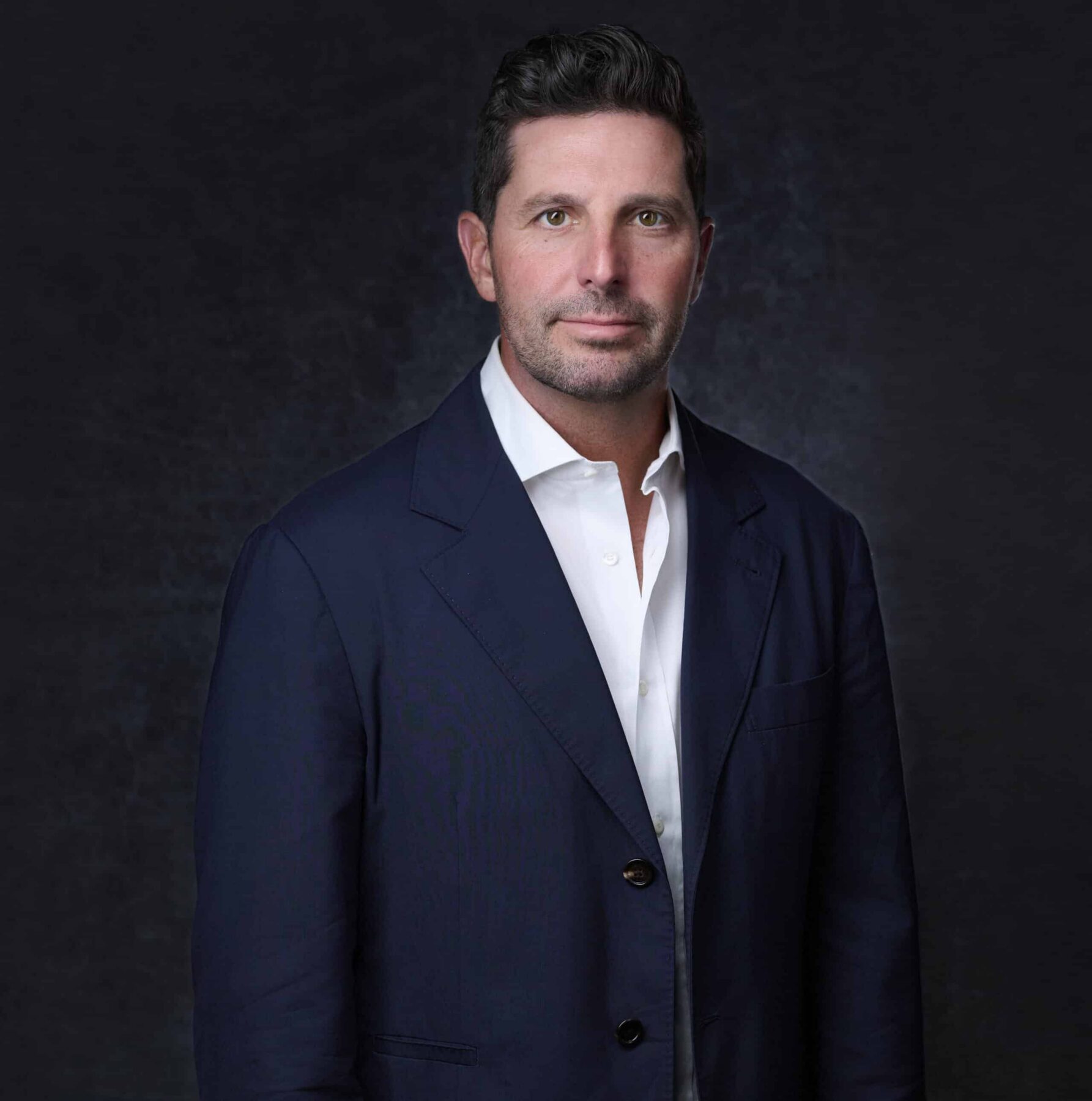MacLaren "Mac" Cummings stands in a navy suit against a dark background