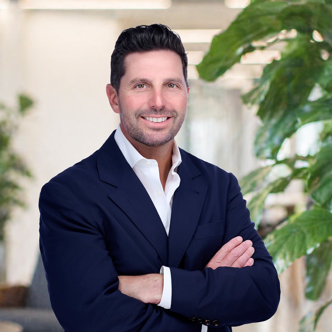 MacLaren "Mac" Cummings smiles in a suit with his arms folded across his chest.