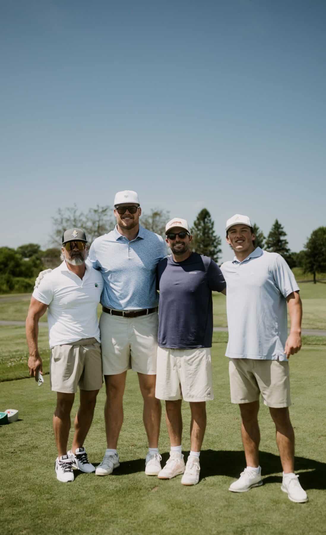 Four men stand on a golf course, smiling